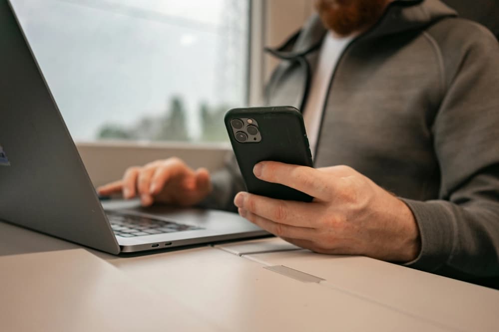 Male hands are typing on a laptop and with his phone in hand